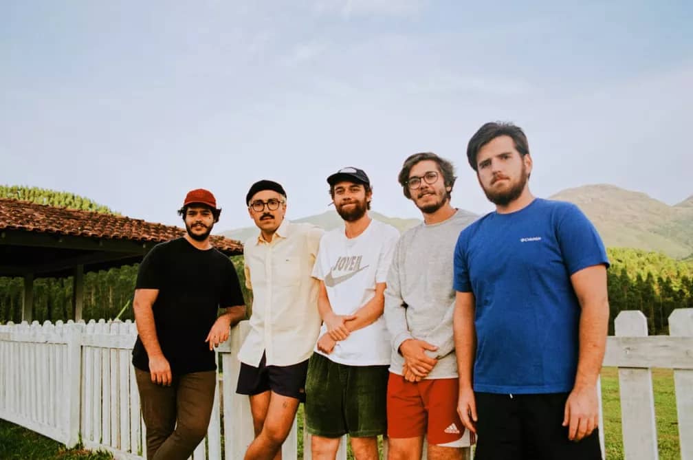 Foto dos cinco integrantes da Banda Jovem Dionisio, donos do hit "Acorda, Pedrinho", posando para foto, encostados em uma cerca branca ao que parece ser um chácara.