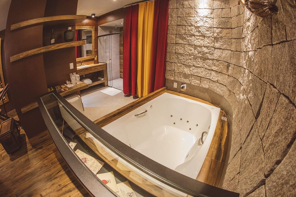 Imagem de suíte de motel inspirada em Harry Potter com hidromassagem retangular, e cortina nas cores da Grifinória (vermelho e Amarelo)