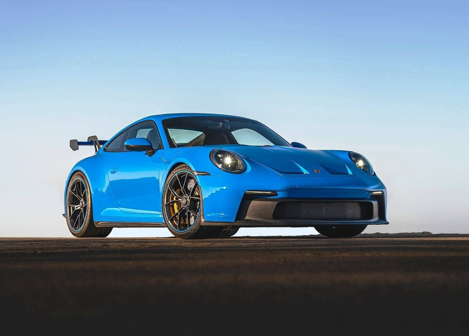 Carro Porsche 911 GT3 na cor azul com faróis ligados. Ao fundo o céu claro também azulado combinando com as cores do carro.