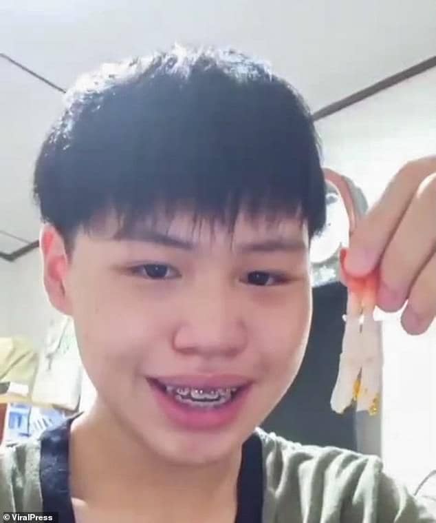 Imagem de garoto tailandês de 21 anos com semblante feliz, sorrindo, usando aparelho dental e camiseta segurando com uma das mãos seu suchi fluorescente