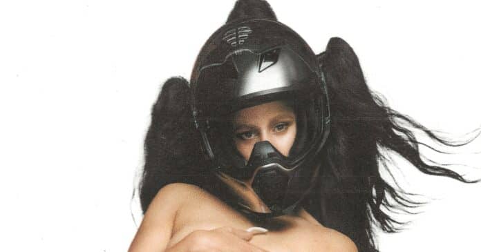 Imagem da cantora Rosalía sobre o fundo branco, usando um capacete preto, aparentemente sem roupa e com asas negras de anjo