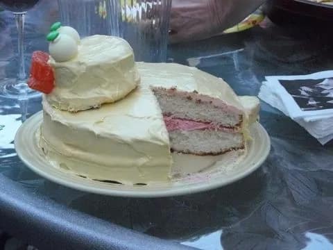 Foto do primeiro bolo de chá de revelação da história. O bolo tem cobertura branca e recheio cor de rosa. Informando que era uma que estava à caminho.